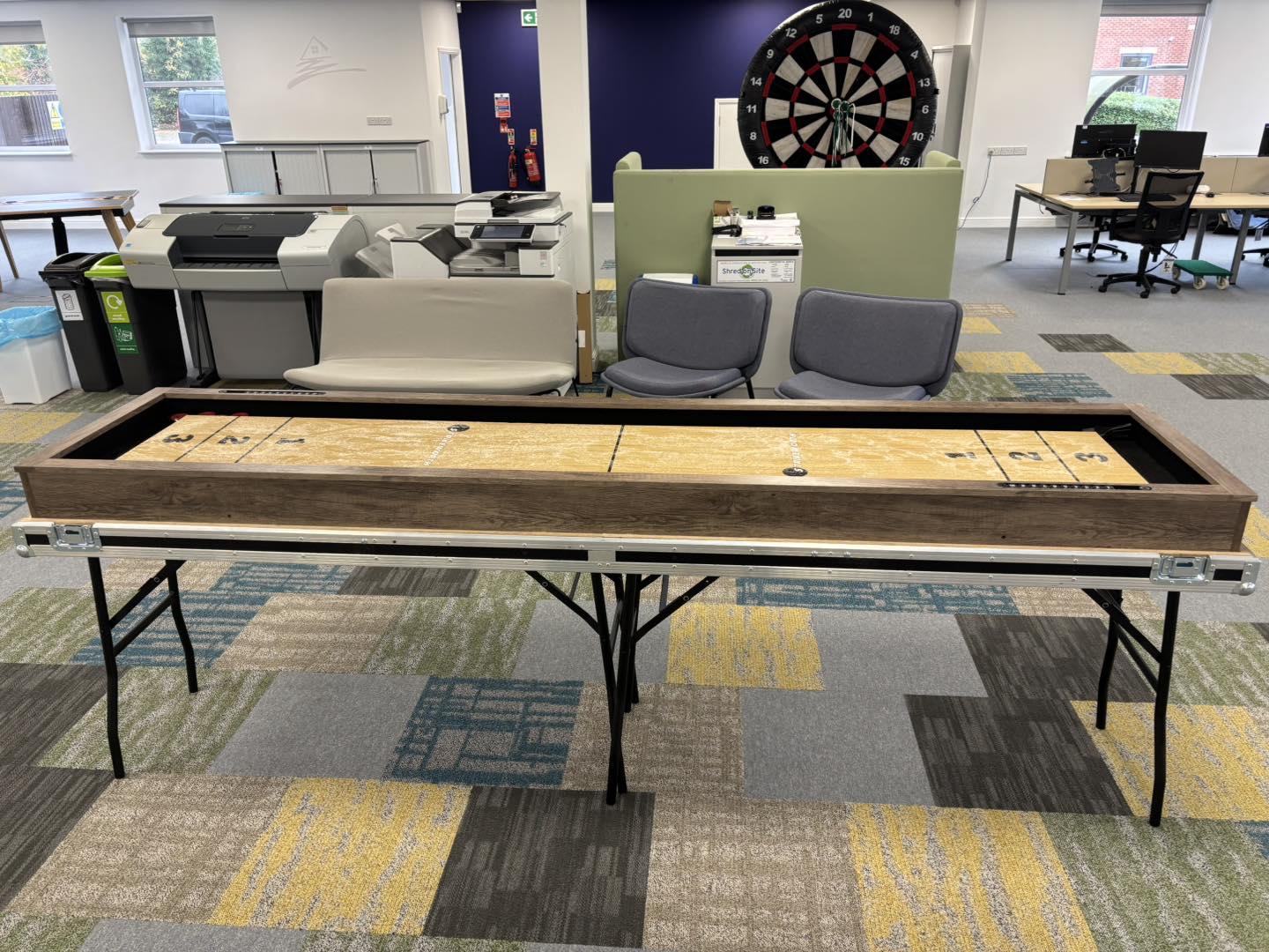 This image shows a shuffleboard table and inflatable velcro darts game on hire at a corporate fun day event in Frodsham.